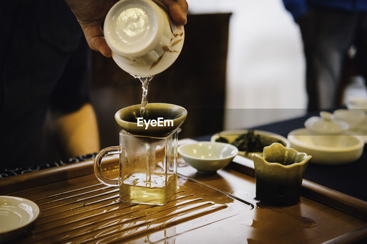 Cropped hand pouring drink in glass on table