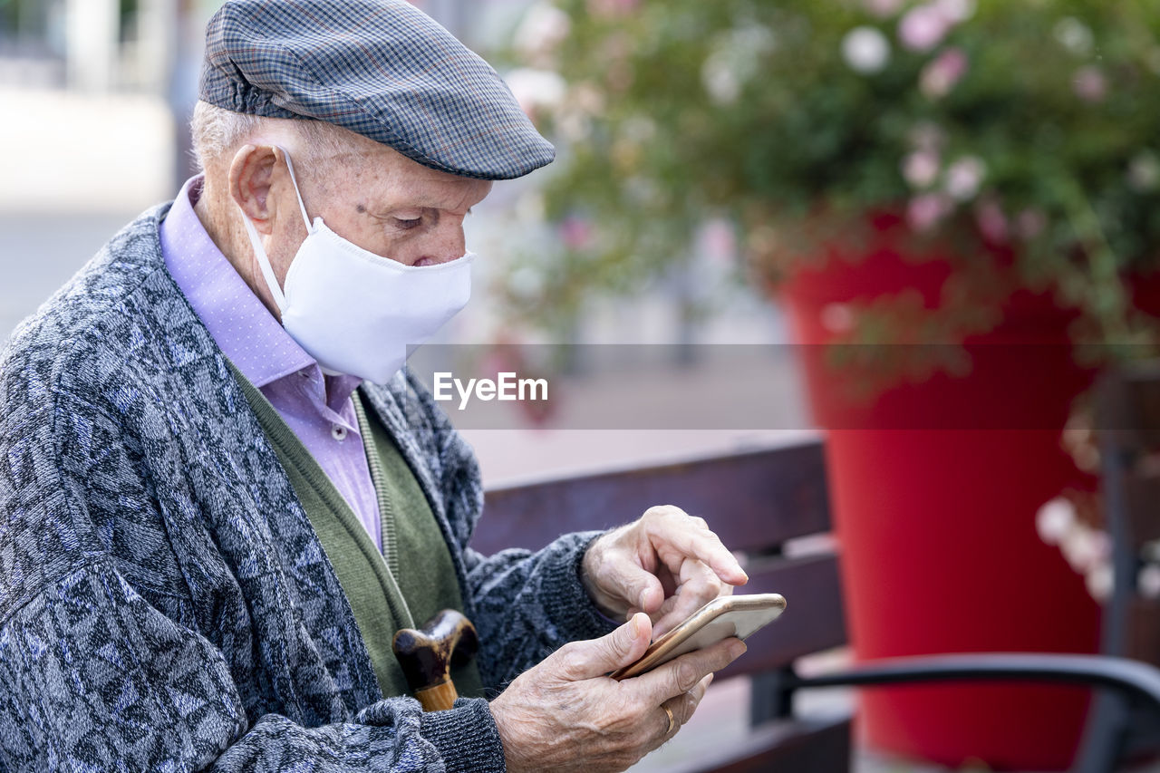 Active senior man using smart phone sitting on bench outdoors