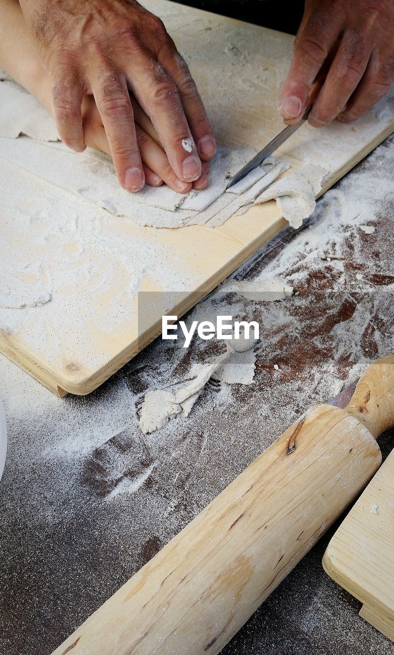 Cropped image of hands cutting pasta on board in kitchen