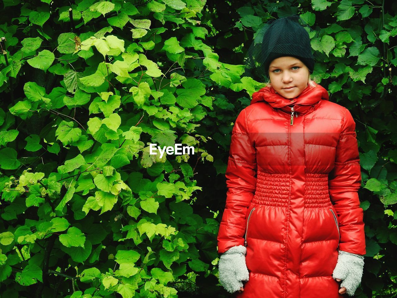 Portrait of girl in red jacket standing against plants