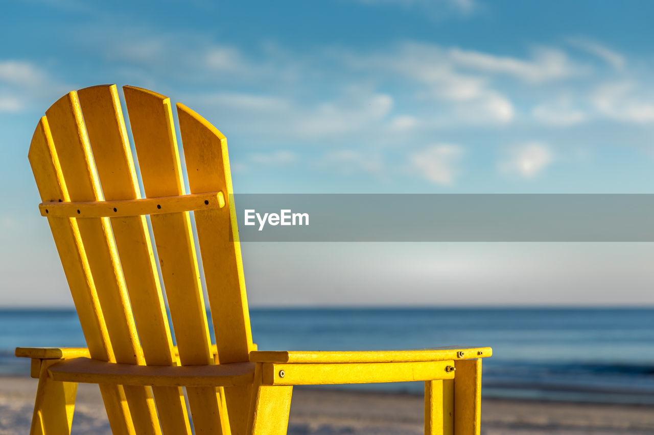 Bright yellow chair  on beach against sky
