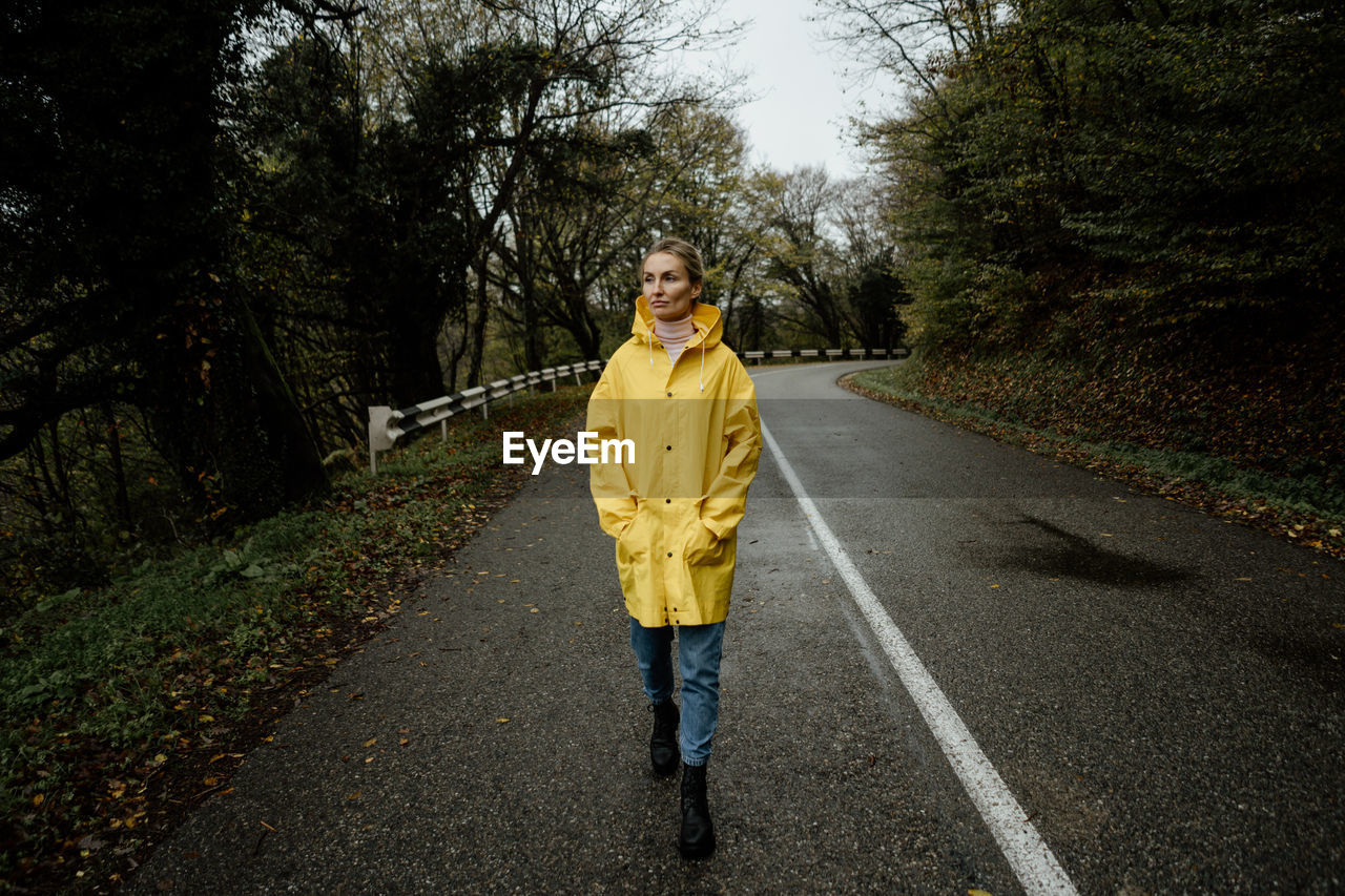 A serene middle-aged woman in a yellow raincoat walks in rainy weather in the countryside.