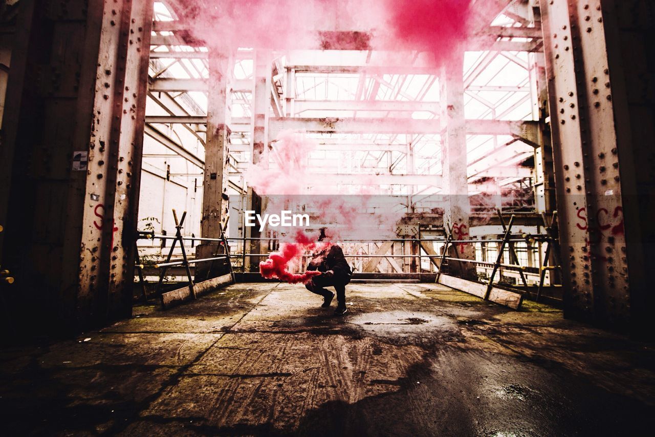 Man crouching with red smoke in metallic structure