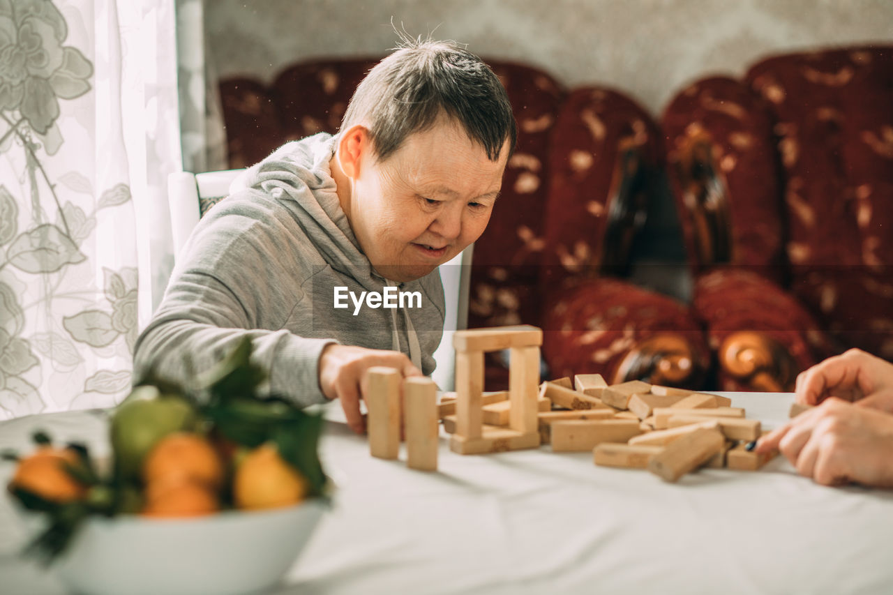 An elderly woman with down syndrome builds towers of their wooden toy blocks