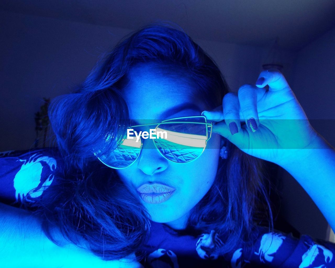 Young woman wearing sunglasses puckering lips in blue illuminated room