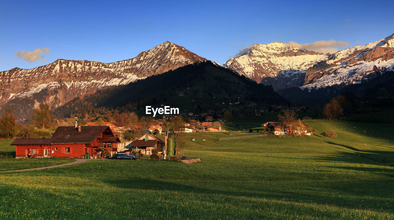 HOUSES ON FIELD BY MOUNTAIN AGAINST SKY