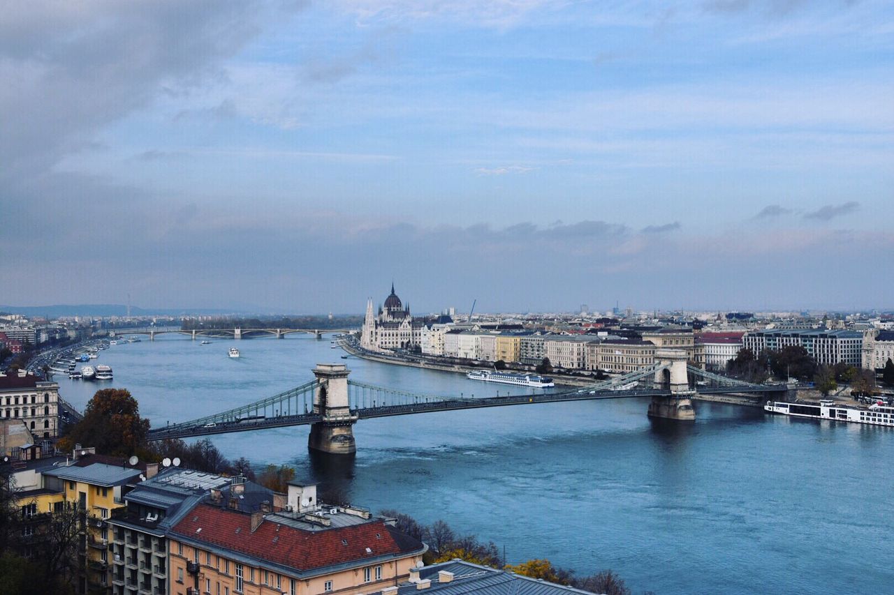 Bridge over river in city against cloudy sky