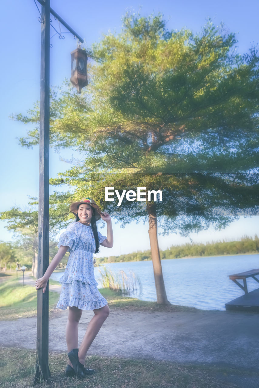 FULL LENGTH PORTRAIT OF YOUNG WOMAN STANDING BY TREES