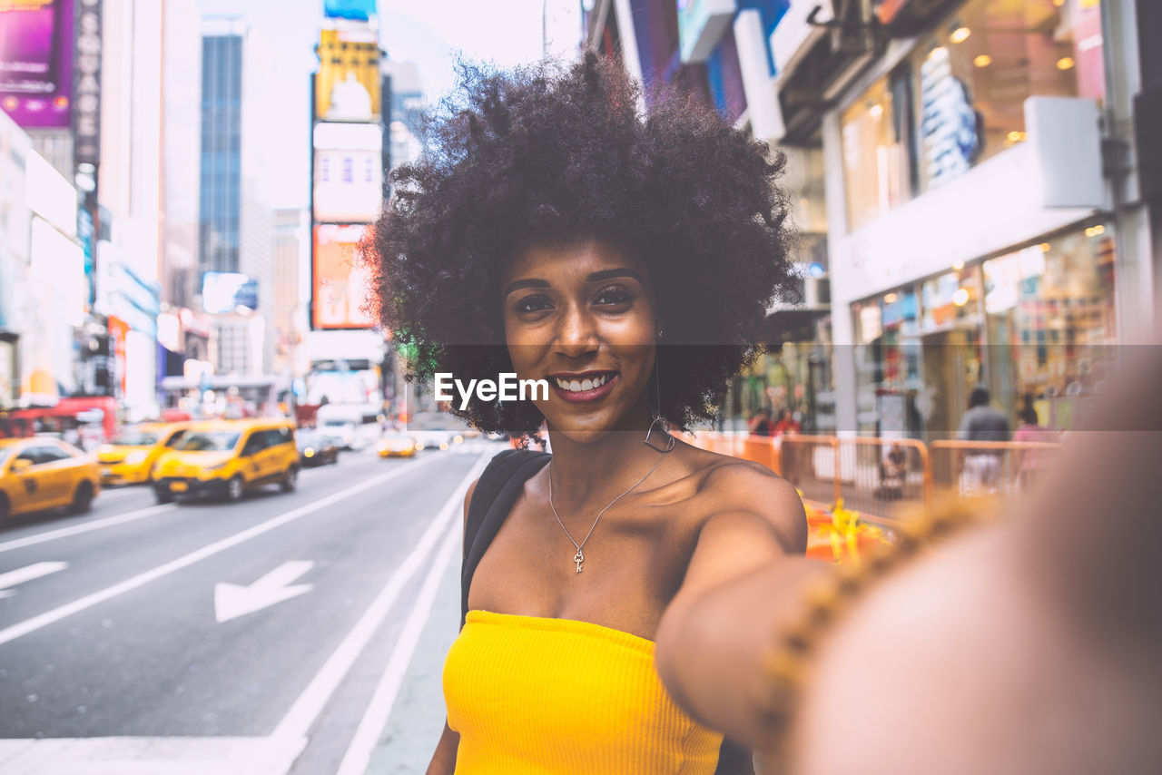 Portrait of happy young woman with afro hairstyle taking selfie on city street