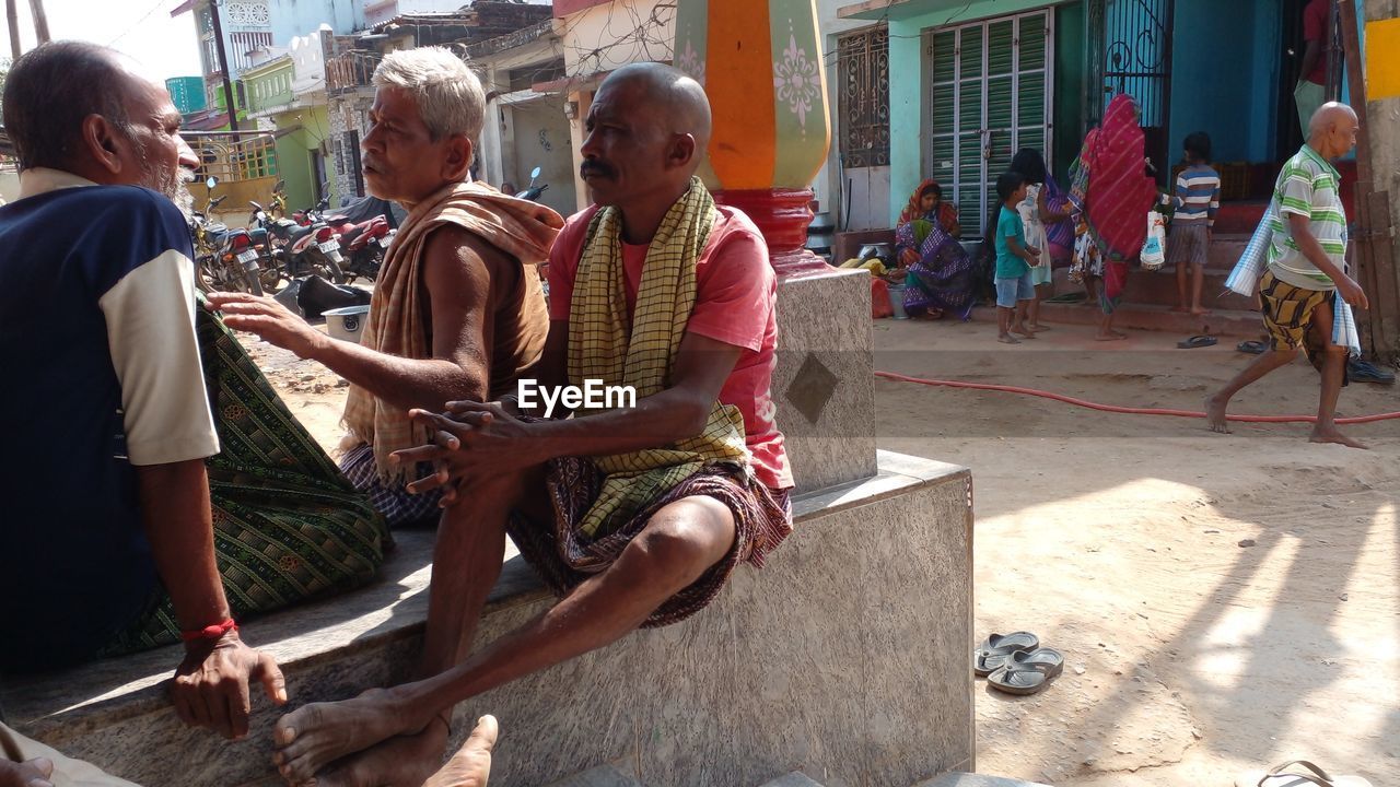 group of people, adult, men, sitting, sunlight, architecture, women, day, casual clothing, lifestyles, city, leisure activity, built structure, nature, building exterior, full length, togetherness, outdoors, friendship, female, senior adult, child, person, street, childhood