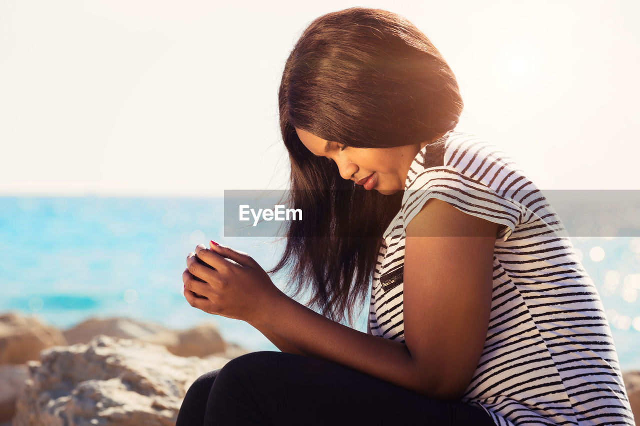 Young woman sitting at beach against sky