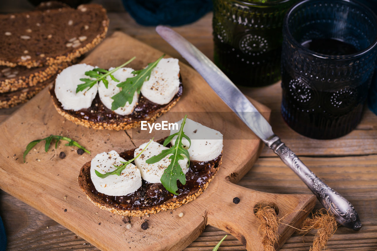 Bruschetta with fig jam, goat cheese and rucola on wooden plate. served with two glasses of red wine