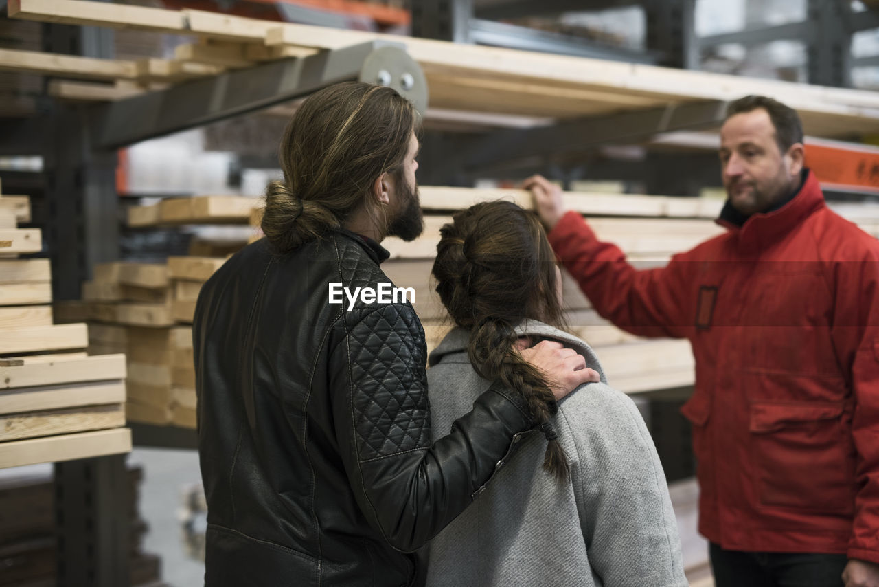 Salesman assisting couple with wooden planks in hardware store
