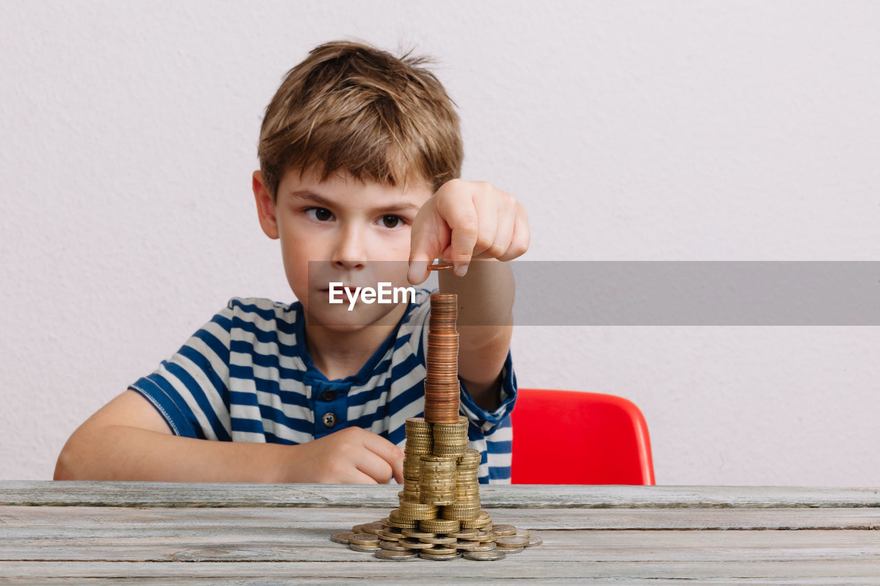 Boy building stack of coins on table against white background
