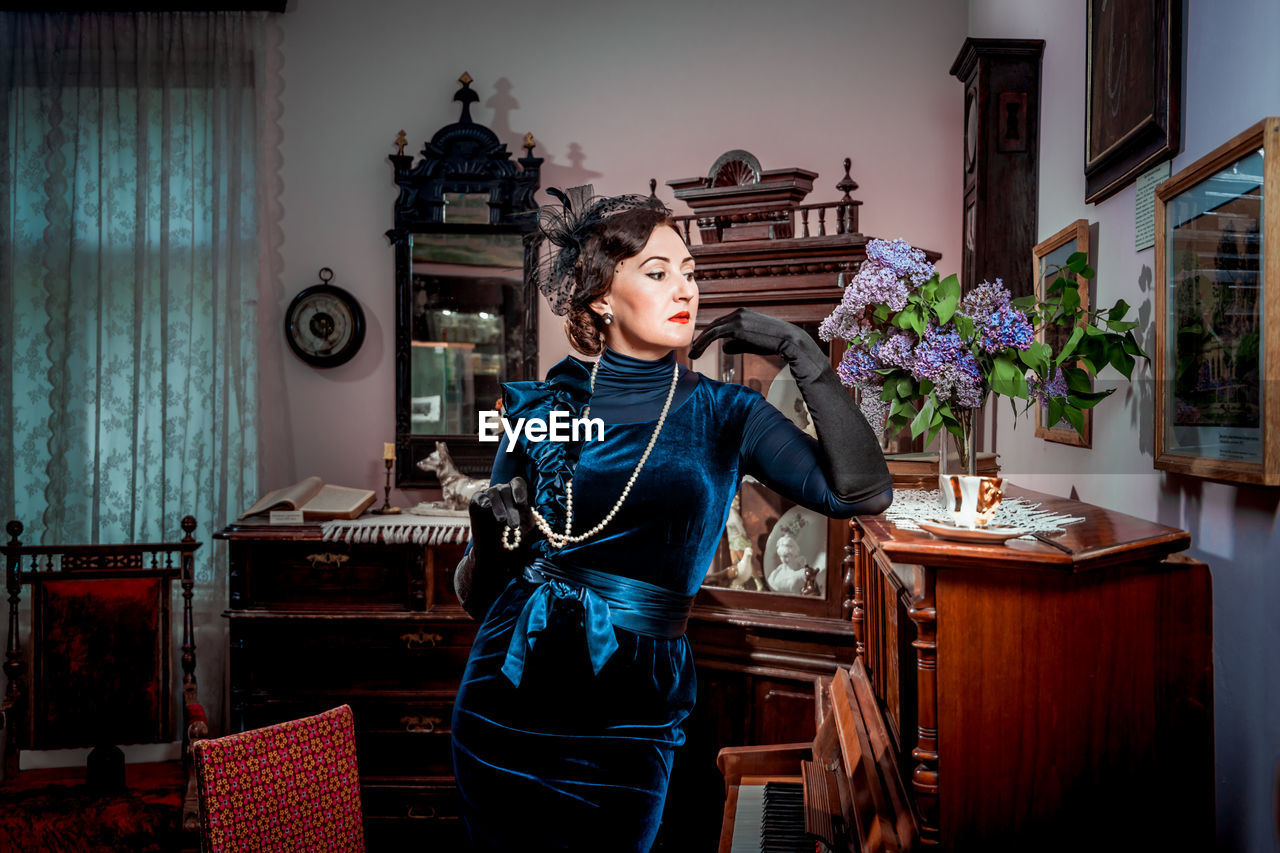Vintage portrait of a stylish lady in an evening dress standing at the piano in retro interior 