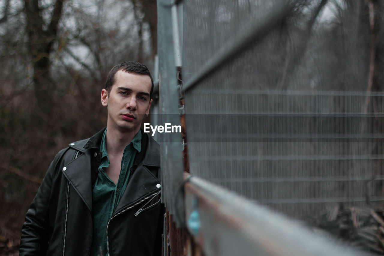 Portrait of young man standing by fence