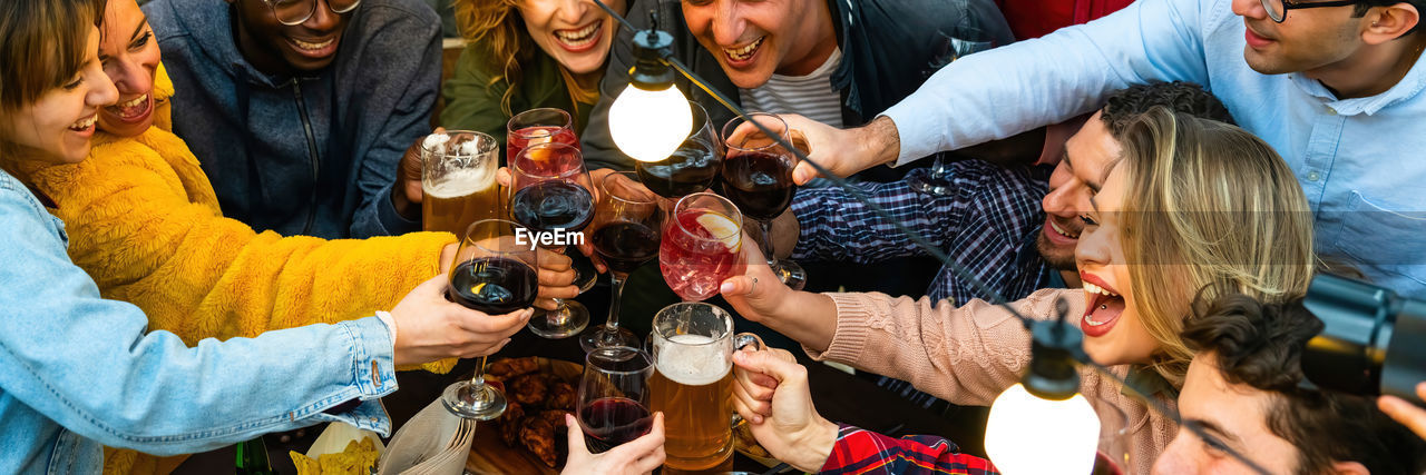 Group of multiracial friends toasting with red wine glasses in terrace restaurant, web banner 