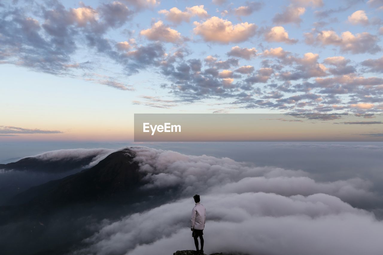 Man standing on cliff looking at cloudscape