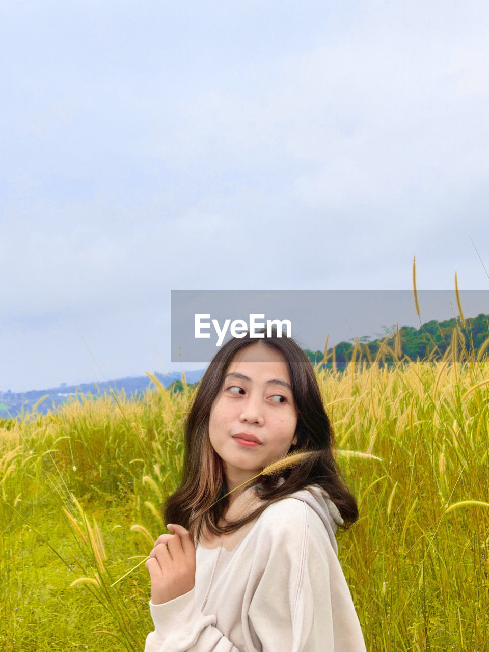 portrait of smiling young woman standing on field against sky