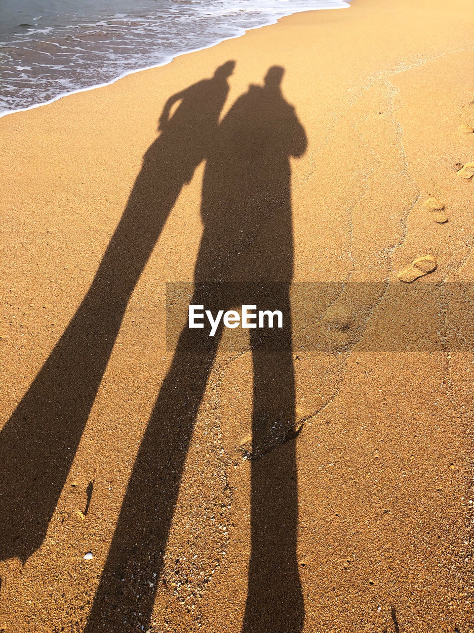 HIGH ANGLE VIEW OF PEOPLE SHADOW ON SAND