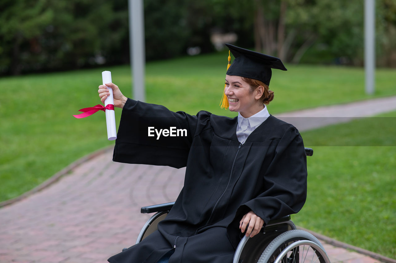 portrait of woman wearing graduation gown standing in park