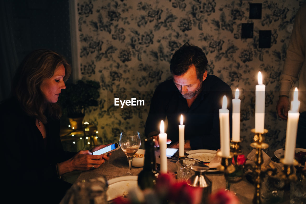 Male and female mature friends using smart phone at dining table in dinner party