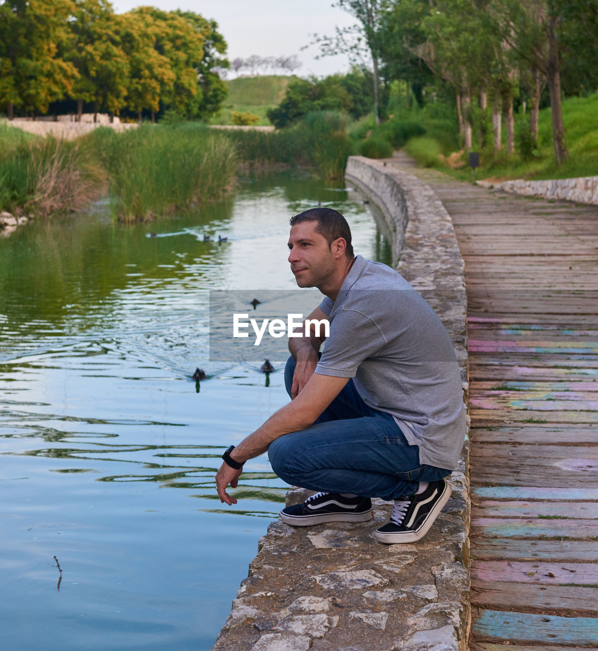 water, one person, men, adult, nature, lake, full length, sitting, side view, plant, tree, casual clothing, day, leisure activity, outdoors, lifestyles, fishing, mature adult, tranquility, looking, animal, occupation, crouching, activity, three quarter length, environment, animal themes, beauty in nature, relaxation, rural scene