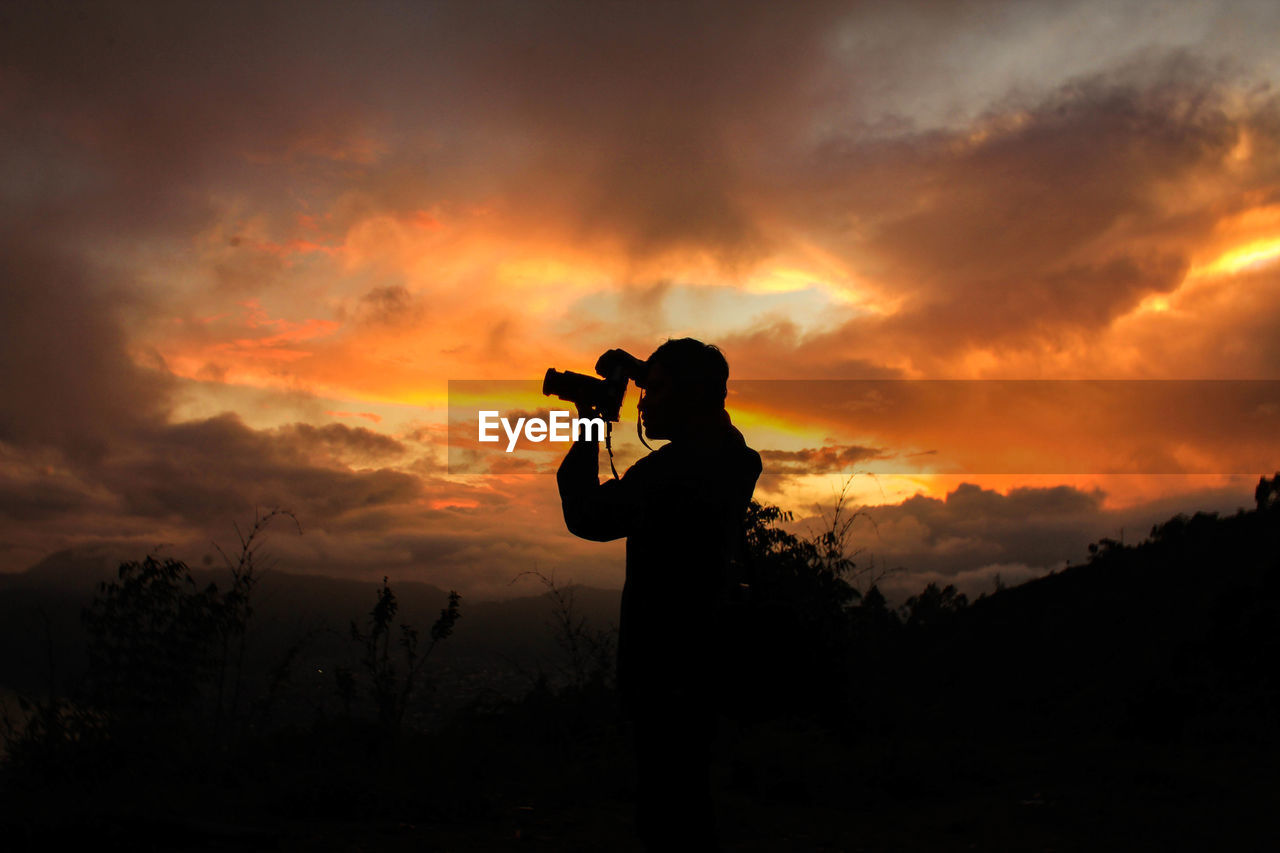 Silhouette man photographing against sky during sunset