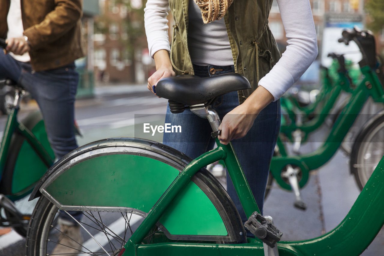 Midsection of woman adjusting bicycle seat while standing with boyfriend at parking lot