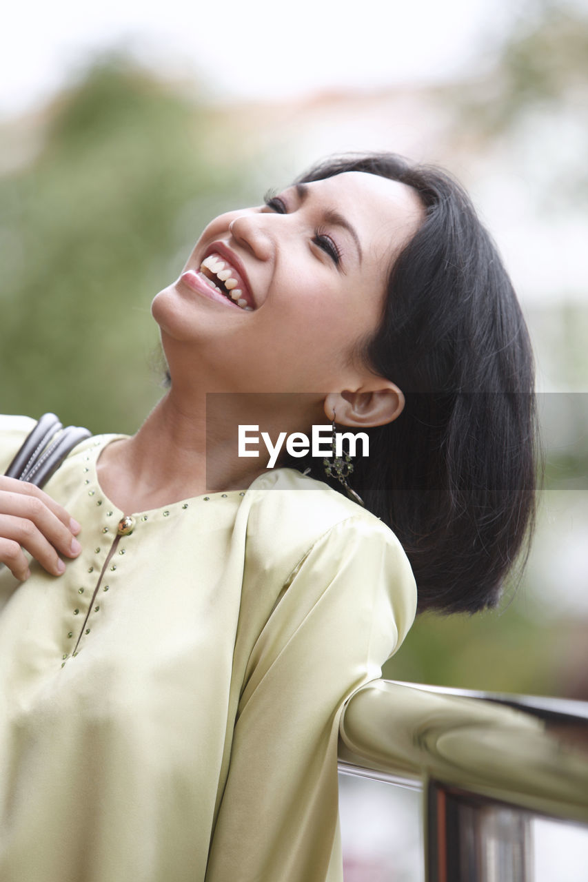 Cheerful woman standing against railing