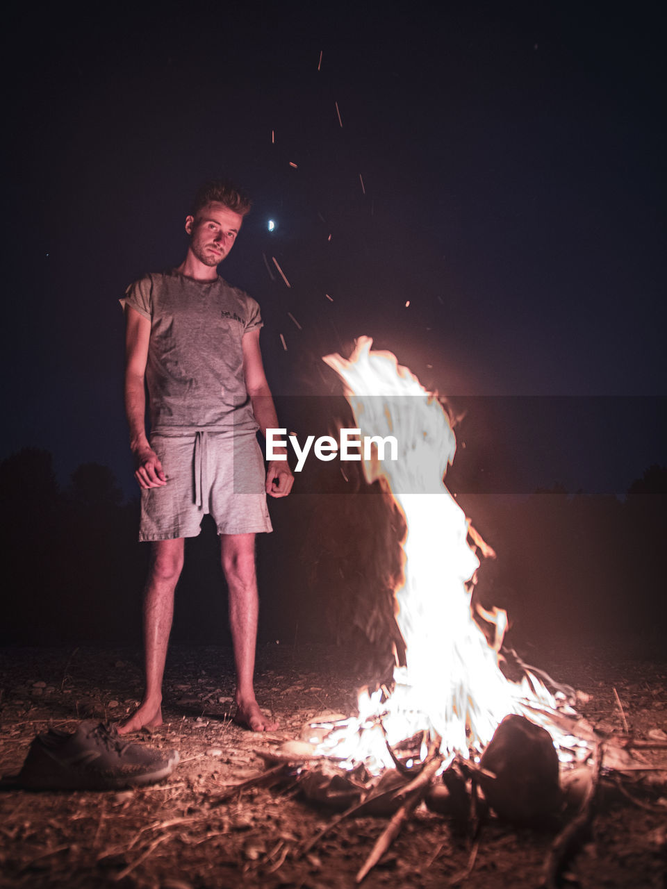 Portrait of man standing by campfire at night