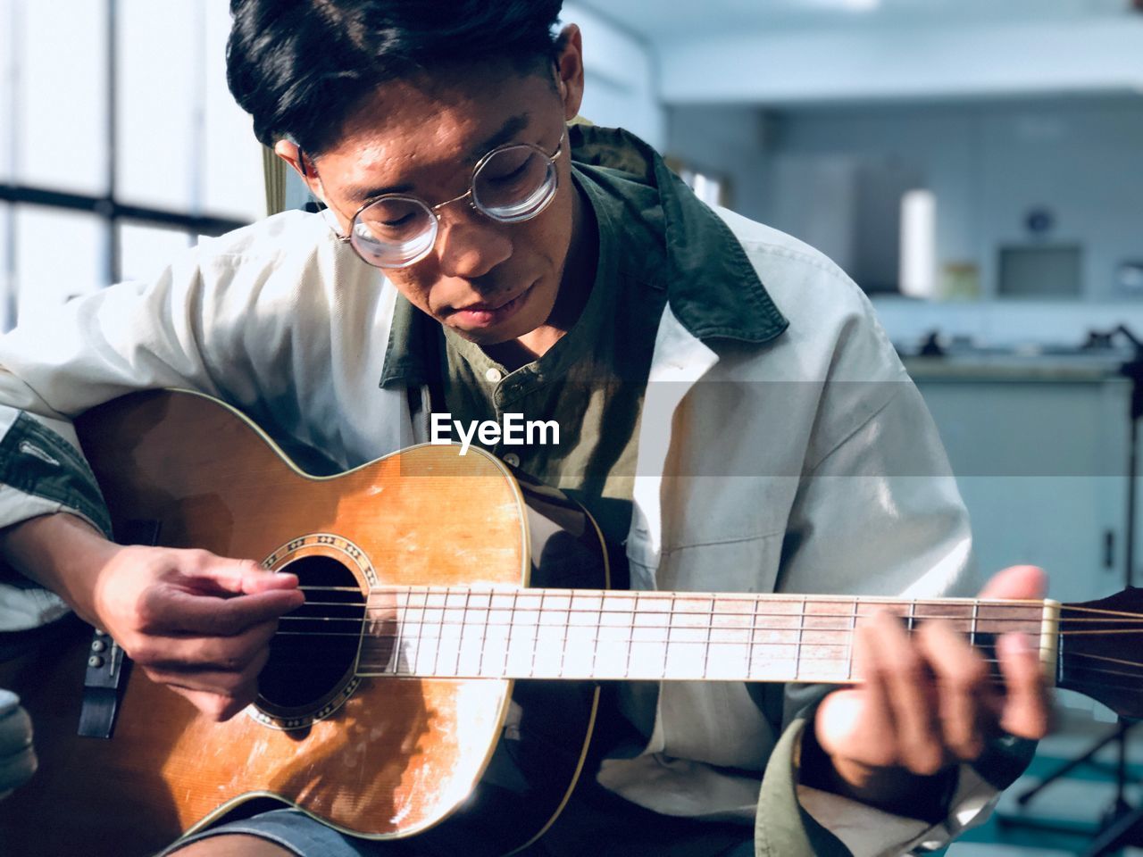 Young man playing guitar while sitting at home