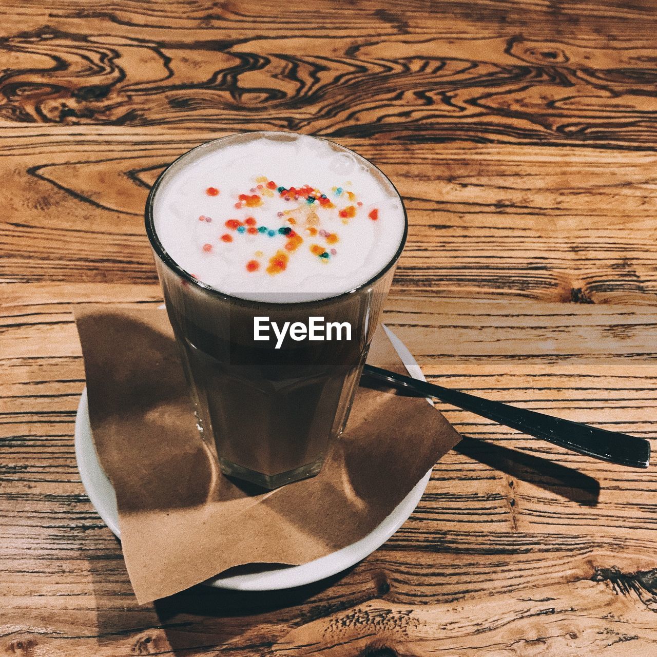 CUP OF COFFEE AND SPOON ON WOODEN TABLE