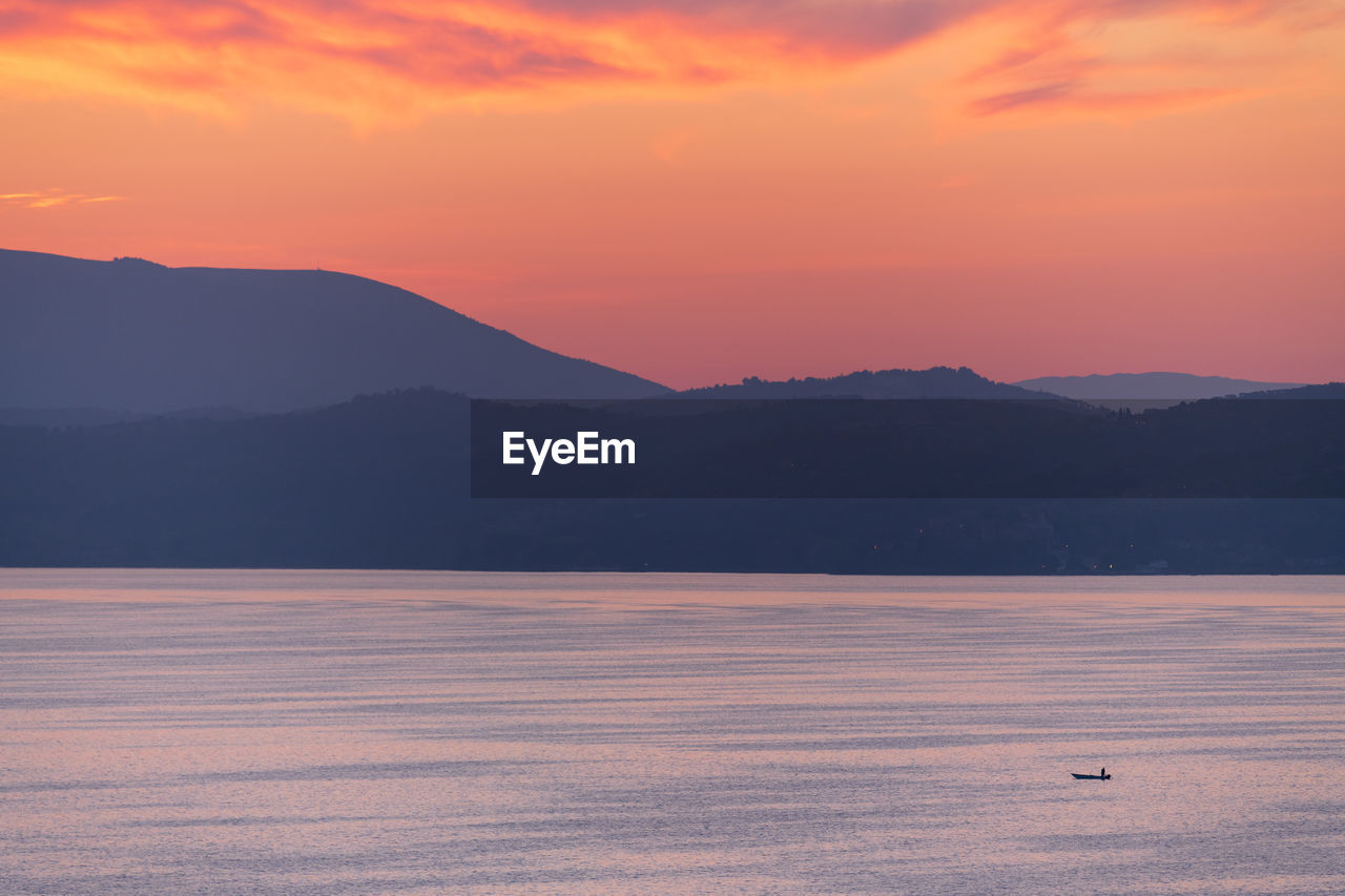 Scenic view of lake and mountains against orange sky