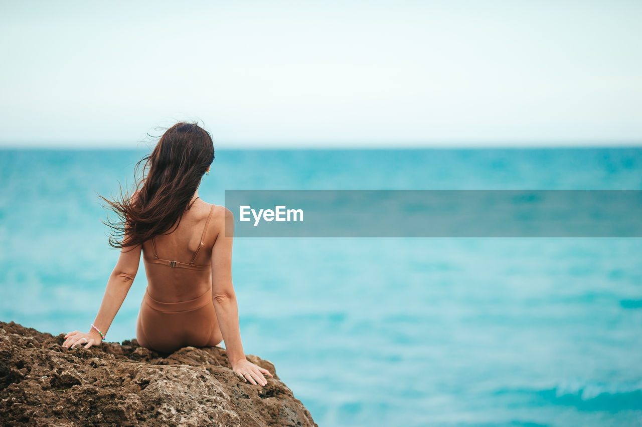 rear view of shirtless man standing at beach against sky