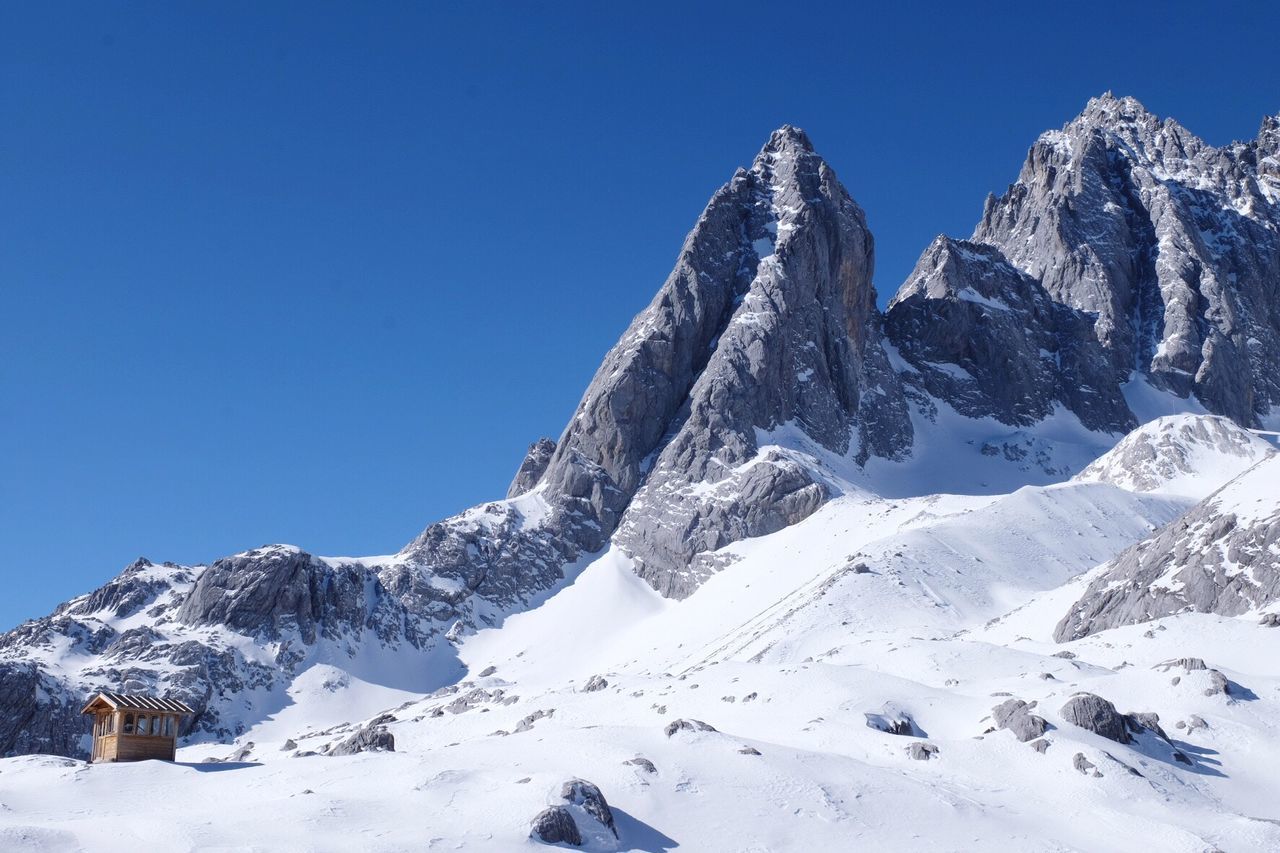 Low angle view of snowcapped mountains against clear blue sky