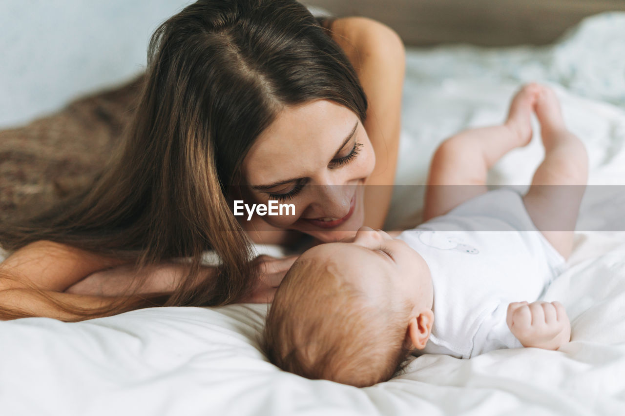 Young mother having fun with cute baby girl on bed, natural tones, love emotion