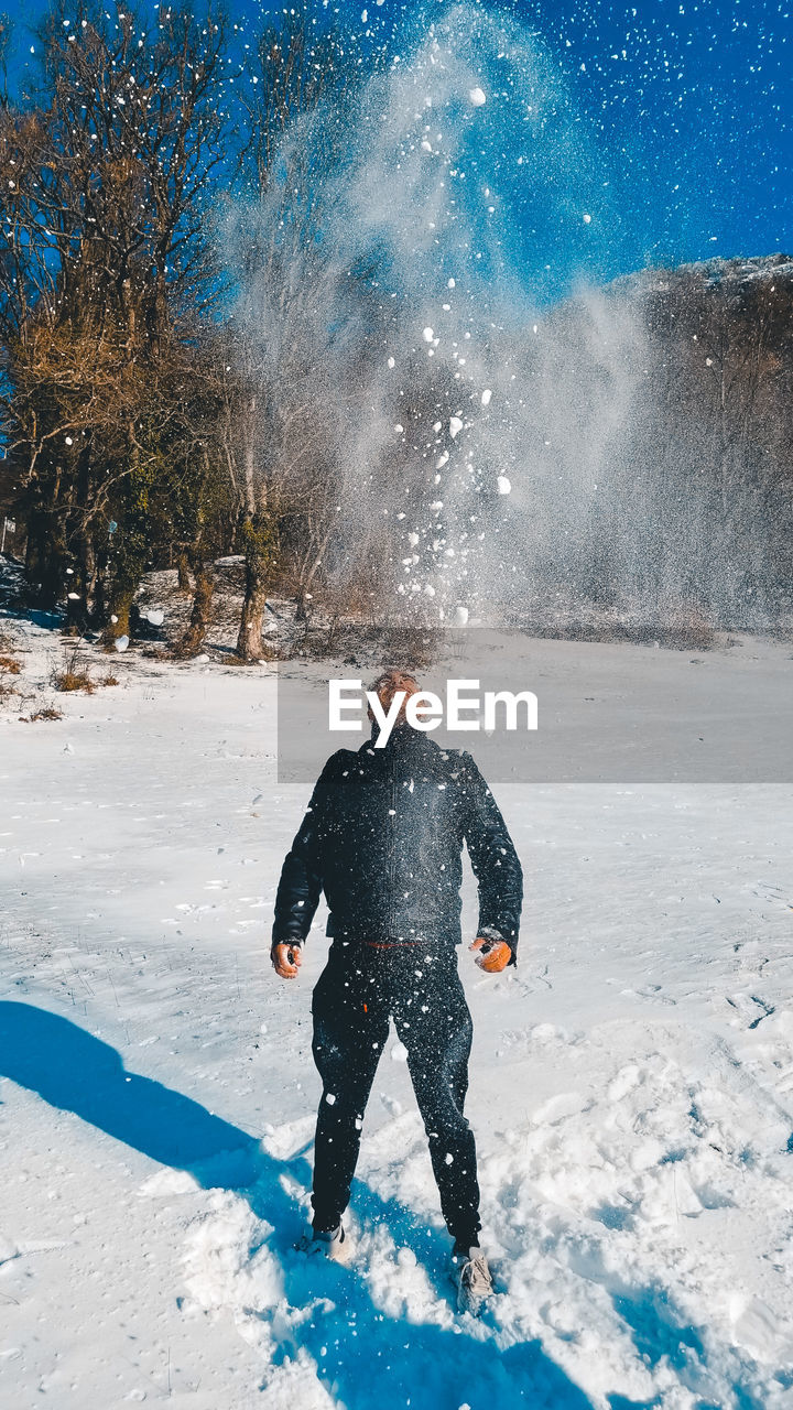 REAR VIEW OF MAN STANDING ON SNOW FIELD