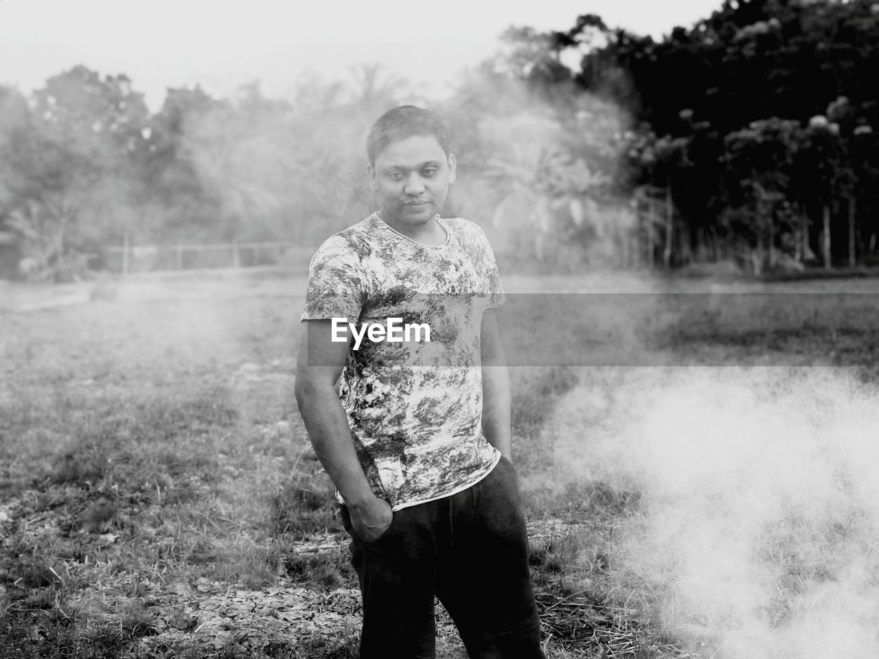 Thoughtful man standing by smoke on field against trees