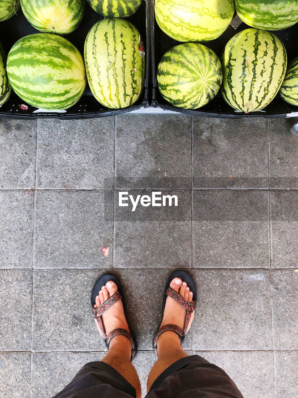 Low section of man standing on tiled floor with melons