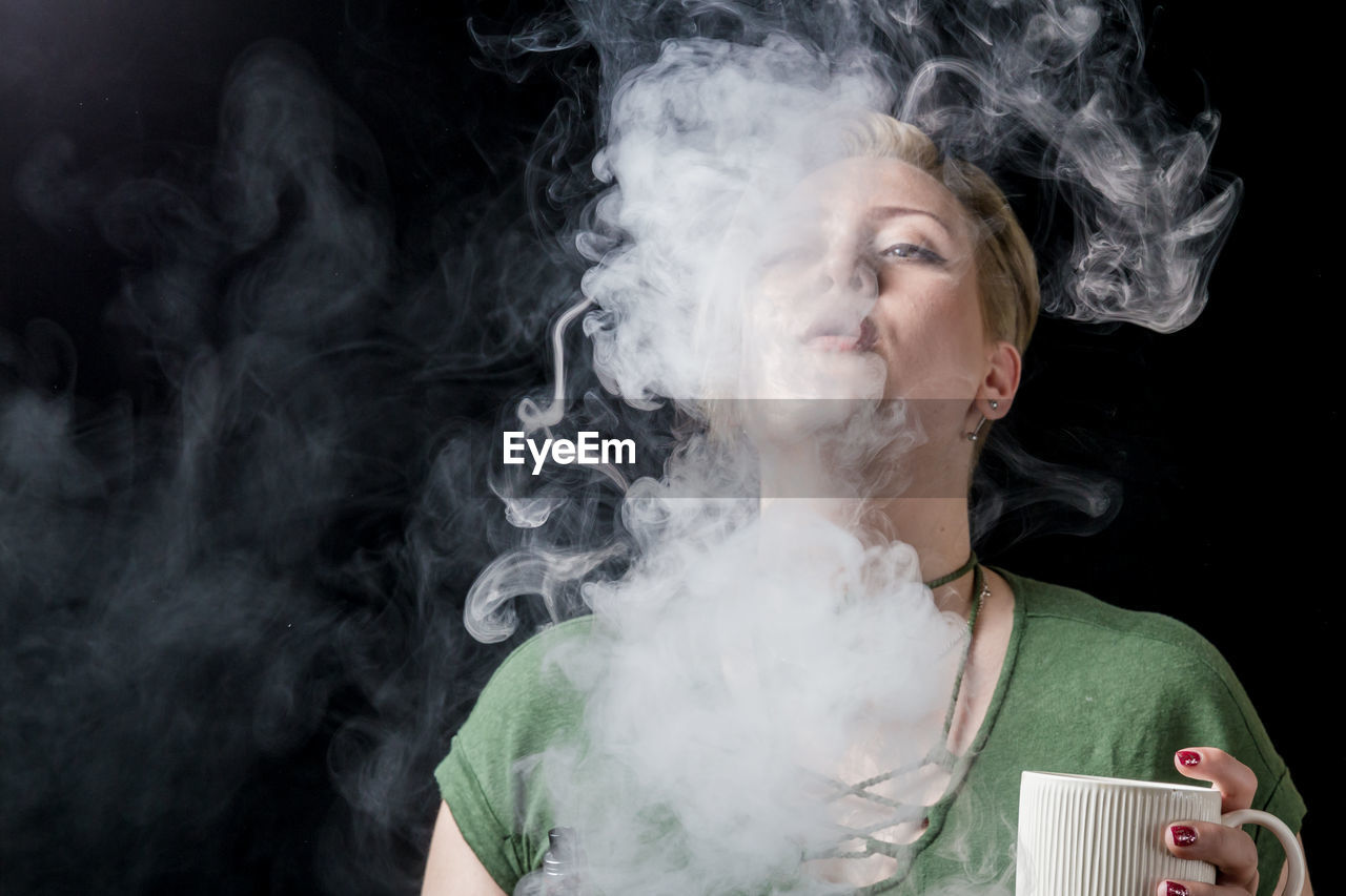 Close-up of woman smoking against black background