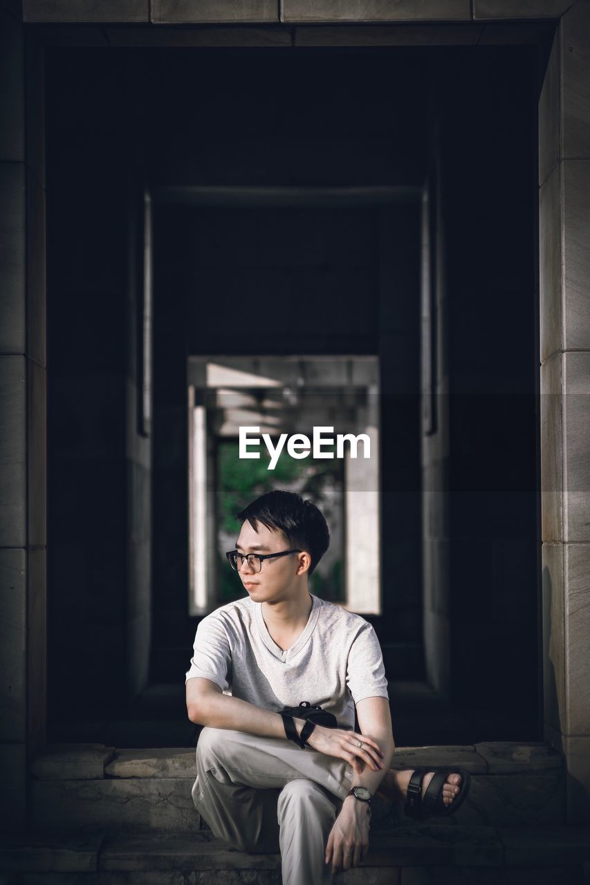 Young man looking away while sitting on staircase