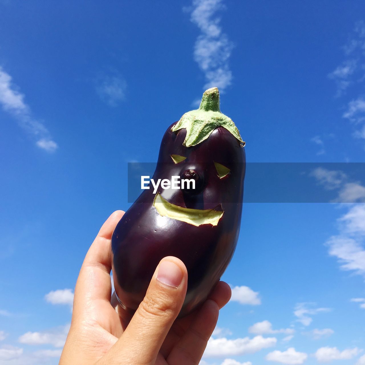 Cropped hand of person holding eggplant against blue sky
