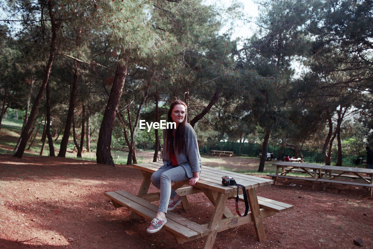 Full length of young woman sitting on picnic table at park