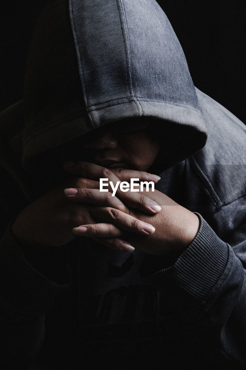 Close-up of woman in hood clothing against black background