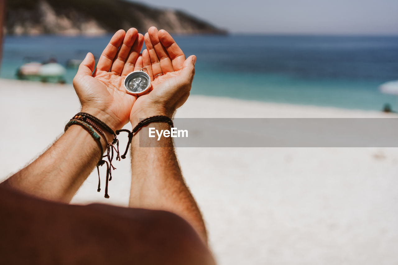 Cropped image of man holding navigational compass at beach