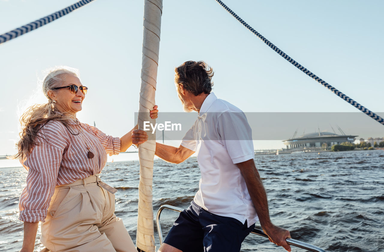 Smiling couple standing on boat in sea against sky