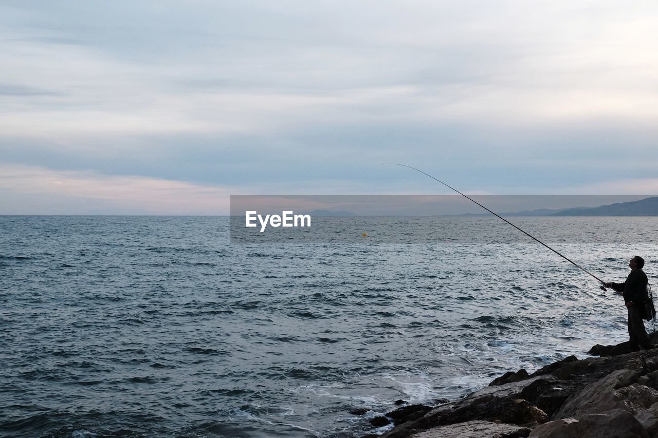 Man fishing in sea against sky