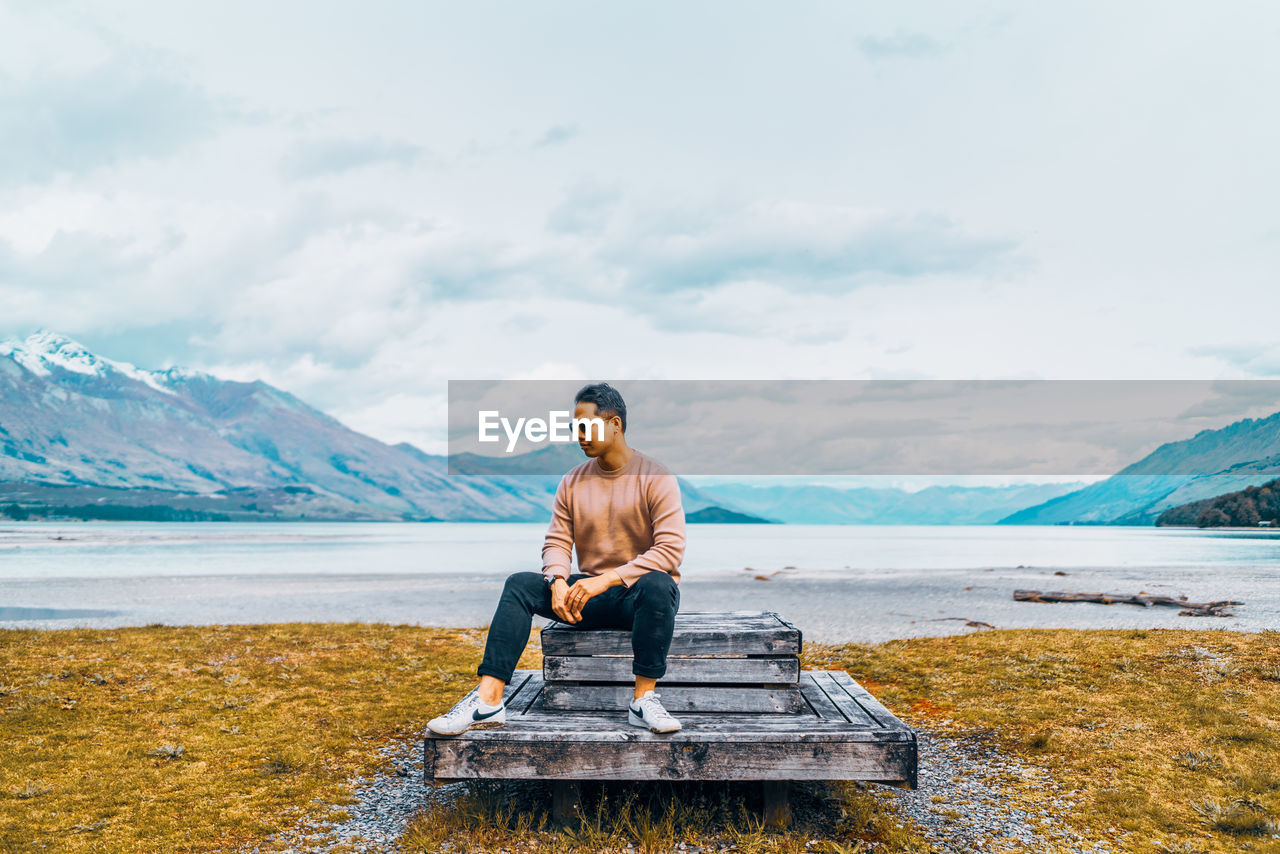 Full length of man sitting on lake against mountains