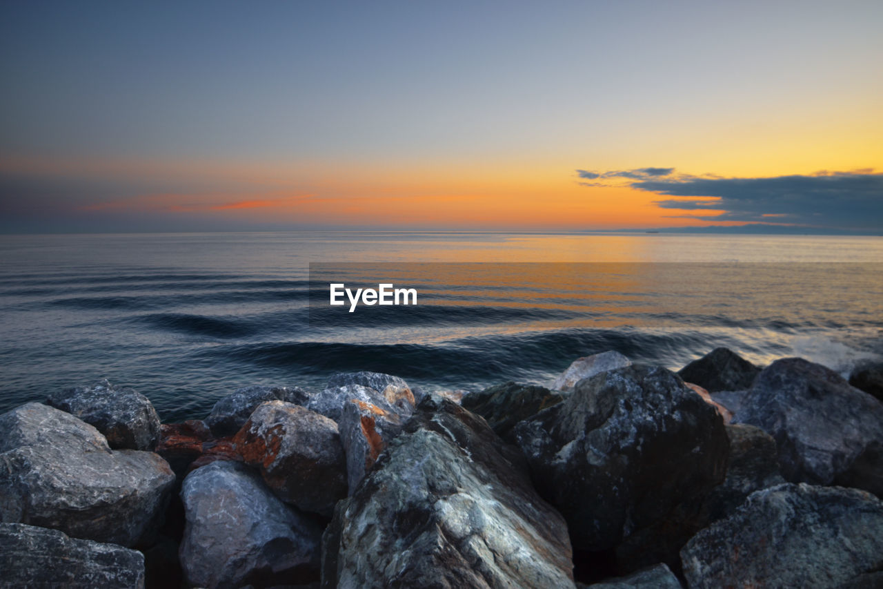 SCENIC VIEW OF ROCKS AT BEACH DURING SUNSET
